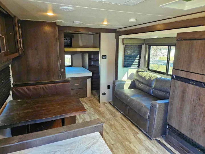 Step inside this RV rental's living area! Features a dinette, comfortable sofa, and bunk beds, perfect for your travel trailer adventures.. Grand Design Transcend Xplor 2022
