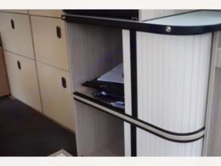 RV rental interior: Light-colored modular cabinets, including one with a unique curved roll-up tambour door for storage.. Ford Triton 2024
