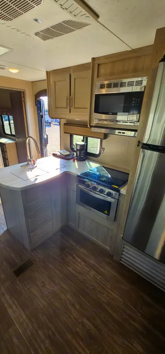 Step inside this clean RV rental kitchen! Features a sink, stove, microwave, and fridge, all in a modern travel trailer.. Forest River Aurora 2022
