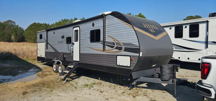 Grey and gold Aurora RV rental travel trailer with steps, hitched to a white truck. Sunny outdoor setting with fields.. Forest River Aurora 2022