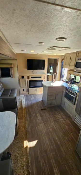 This RV rental interior showcases a modern living area with TV & fireplace, a functional kitchen, and dining booth.. Forest River Aurora 2022