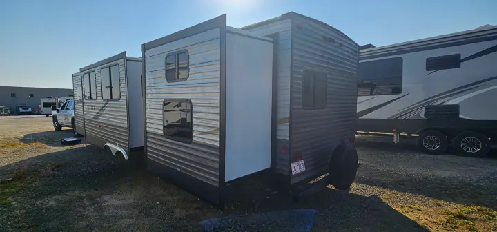 An RV rental travel trailer with its slide-out extended, parked in a sunny outdoor lot beside another large RV.. Forest River Aurora 2022