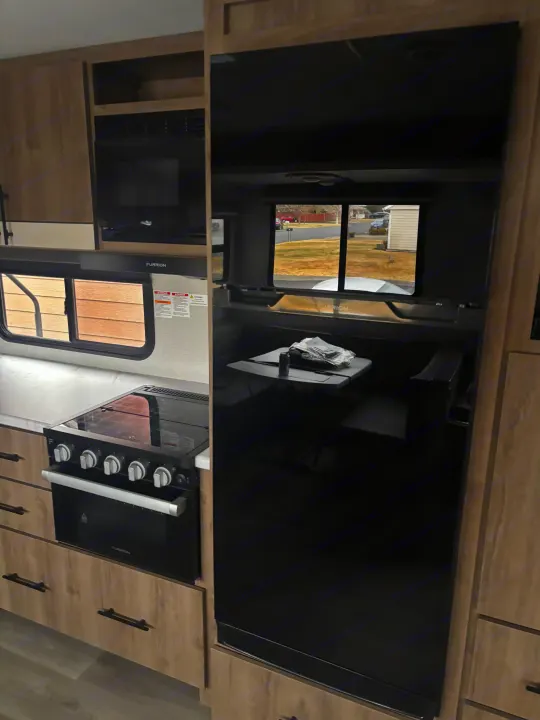 Sleek RV rental kitchen featuring a Furrion stove, microwave, and functional dining space, offering outdoor views.. Grand Design Imagine 2800bh 2025