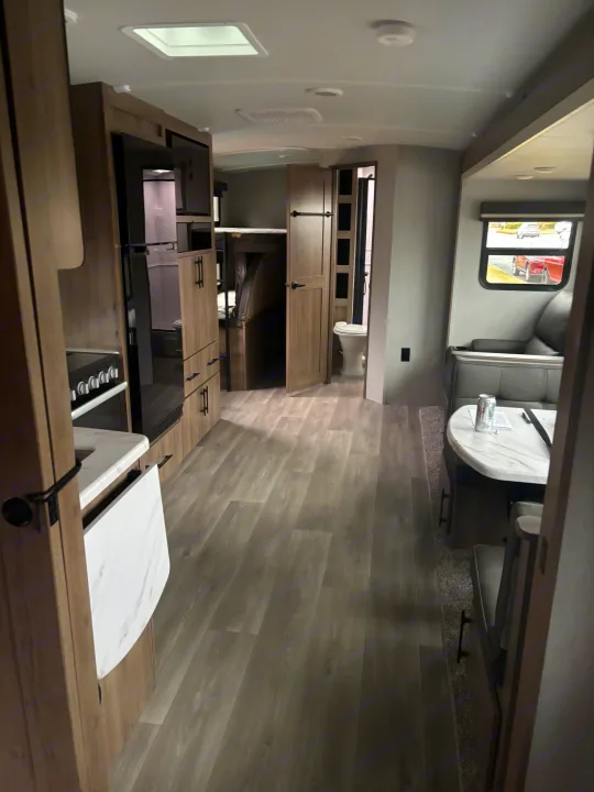 Inside a modern RV rental featuring a light wood kitchen, gray flooring, dining table, and accessible bathroom.. Grand Design Imagine 2800bh 2025