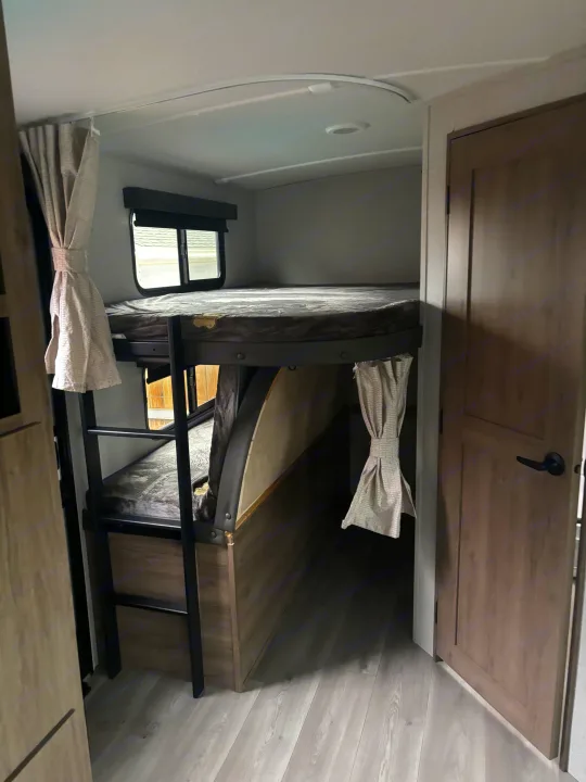 RV rental interior with stacked bunk beds, a ladder, and a window, designed for compact travel comfort.. Grand Design Imagine 2800bh 2025