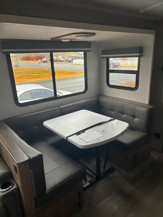 Spacious RV rental dinette featuring comfortable U-shaped seating, a modern white table, and expansive windows with outdoor views.. Grand Design Imagine 2800bh 2025