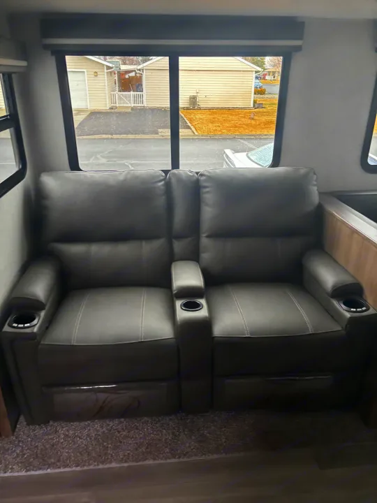 Two comfortable reclining seats with cup holders inside an RV. Windows offer a view of houses, ideal for an rv rental.. Grand Design Imagine 2800bh 2025