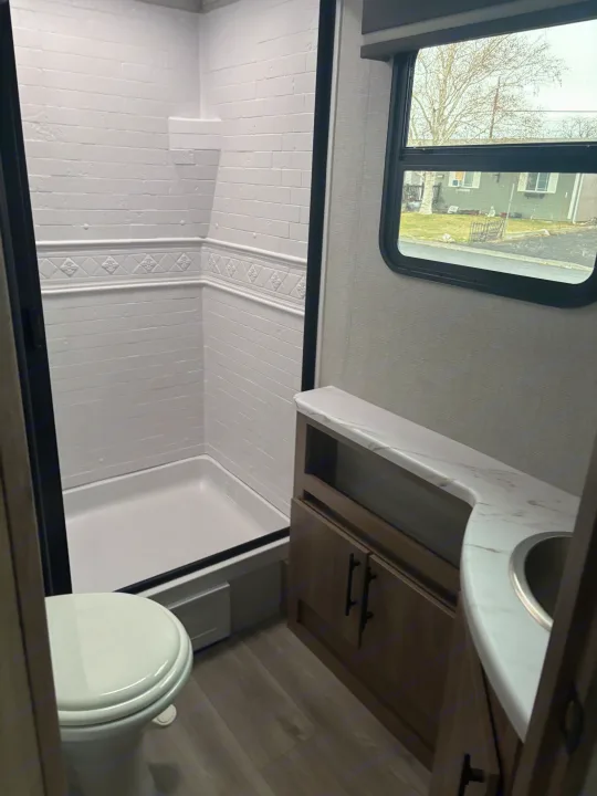 Modern RV rental bathroom: features a white shower with tile-like walls, a vanity, and toilet.. Grand Design Imagine 2800bh 2025