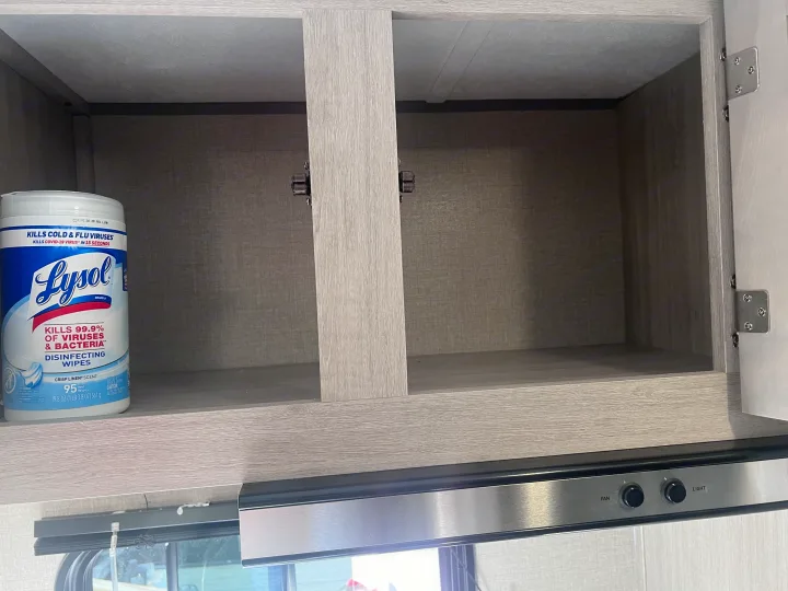 Inside an RV rental, an open cabinet holds Lysol wipes above the kitchen range hood.. Coachmen 164BHX 2023