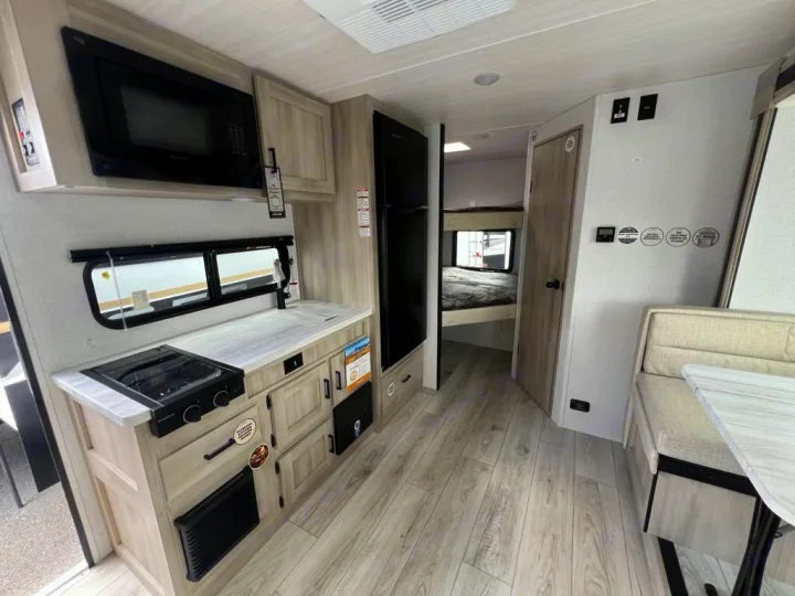 Spacious RV rental interior with a light-toned kitchen, dining booth, and rear bunk beds, offering a complete living space.. East to West Della Terra 181BH 2025