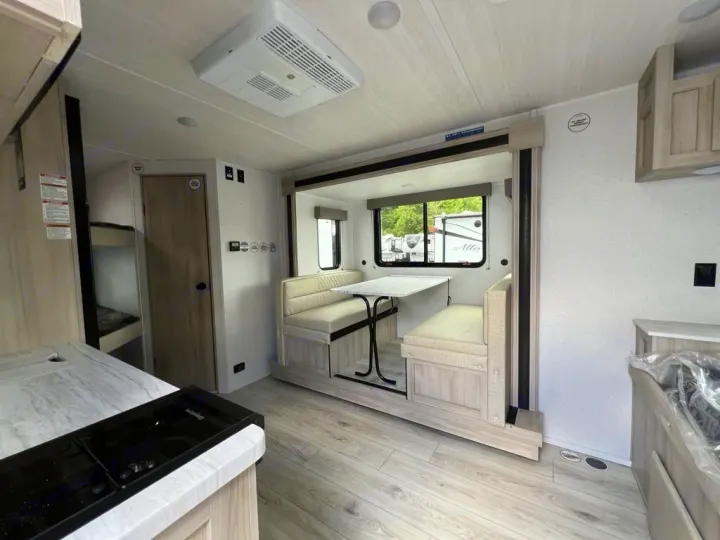 Clean RV rental interior featuring a bright dinette area, kitchen counter, and bunk beds visible through a doorway.. East to West Della Terra 181BH 2025