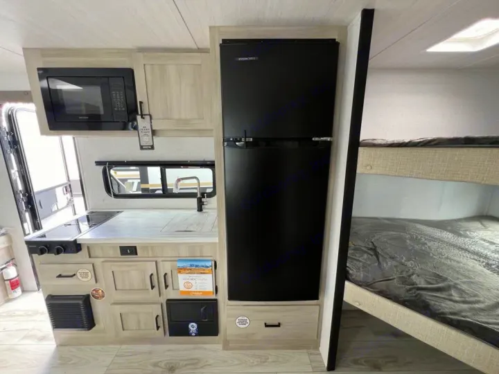 RV rental interior: A compact kitchenette with microwave, stove, sink, large black refrigerator, and bunk beds.. East to West Della Terra 181BH 2025