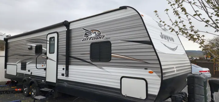 Experience travel with this Jayco Jay Flight RV rental. A grey and white travel trailer with an awning, parked outdoors.. Jayco Jay Flight 2017
