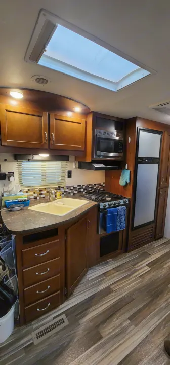 RV rental kitchen galley with sink, stove, microwave, fridge, and ample wood cabinets under a bright skylight.. Jayco Jay Flight 2017
