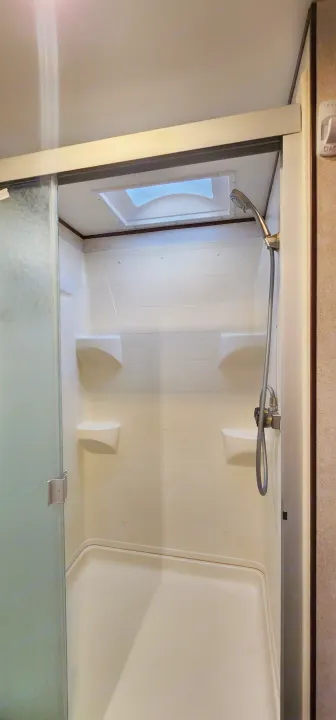 Clean RV rental shower interior: frosted sliding glass door, built-in shelves, handheld showerhead, and overhead skylight.. Jayco Jay Flight 2017