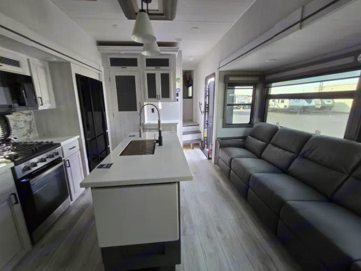 Modern RV rental interior: large kitchen island, black sofa, and light flooring. Ideal for comfortable travel adventures.. Forest River East to West Ahara 390DS 2025