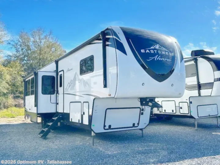 Explore in a modern East West Ahara fifth-wheel RV rental. White with black accents & mountain graphics, parked on gravel.. Forest River East to West Ahara 390DS 2025