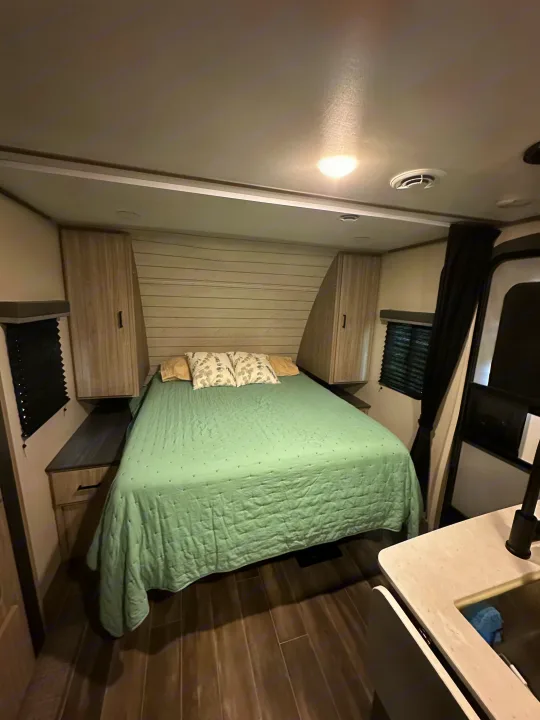 Comfortable RV rental bedroom: light green bedspread, wood paneling, side storage, and ceiling lights.. Keystone RV Passport SL 2022