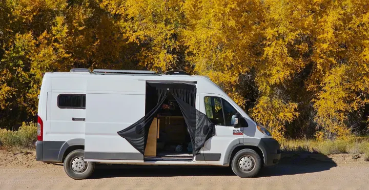 Fall rv rental adventure: a white camper van with an open door, parked on a dirt road against stunning yellow autumn trees.. RAM Promaster 2500 159wb 2018