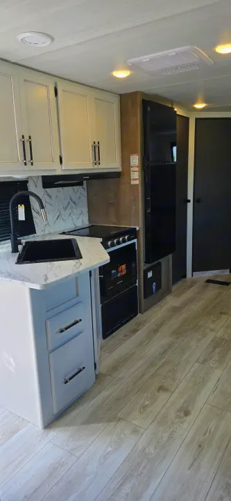 Modern RV rental kitchen featuring light cabinets, black appliances, sink, and stove in a bright interior.. Keystone Springdale 2025