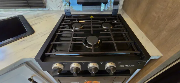 Modern RV rental kitchen featuring a black Contoure gas stove with four burners, integrated sink, and white countertop.. Keystone Springdale 2025