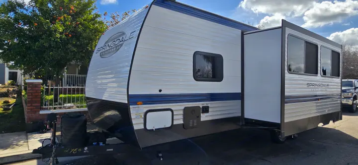 A white and blue Springdale travel trailer RV rental, seen outdoors with its slide-out extended.. Keystone Springdale 2025