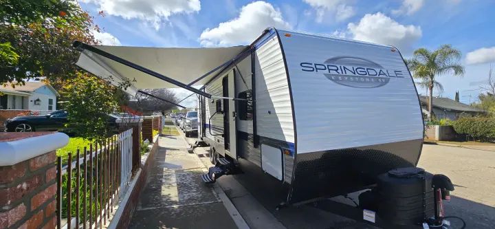 A white Springdale Keystone travel trailer with its awning extended, parked roadside for an RV rental adventure.. Keystone Springdale 2025