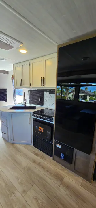 Modern RV rental with a fully-equipped kitchen featuring a sink, stovetop, microwave, and integrated appliances.. Keystone Springdale 2025