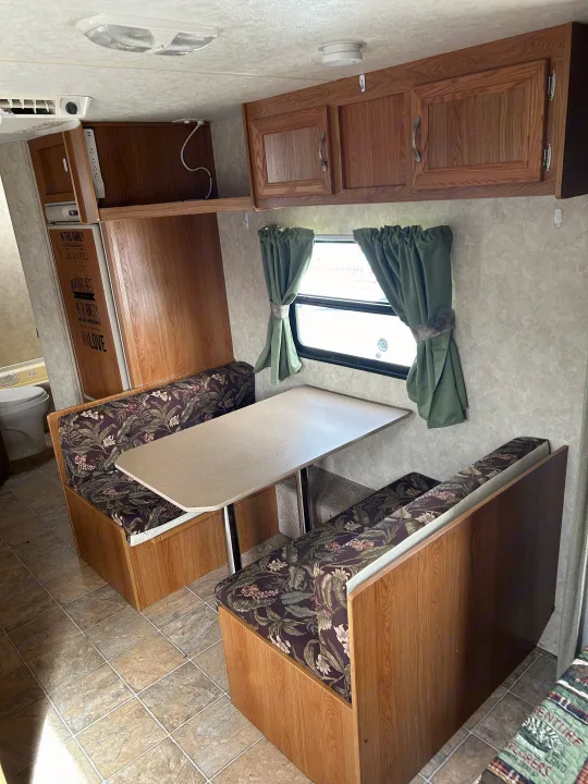 Spacious RV rental interior featuring a cozy dinette with floral upholstery, overhead storage, and ample natural light.. Jag Jag II 2007