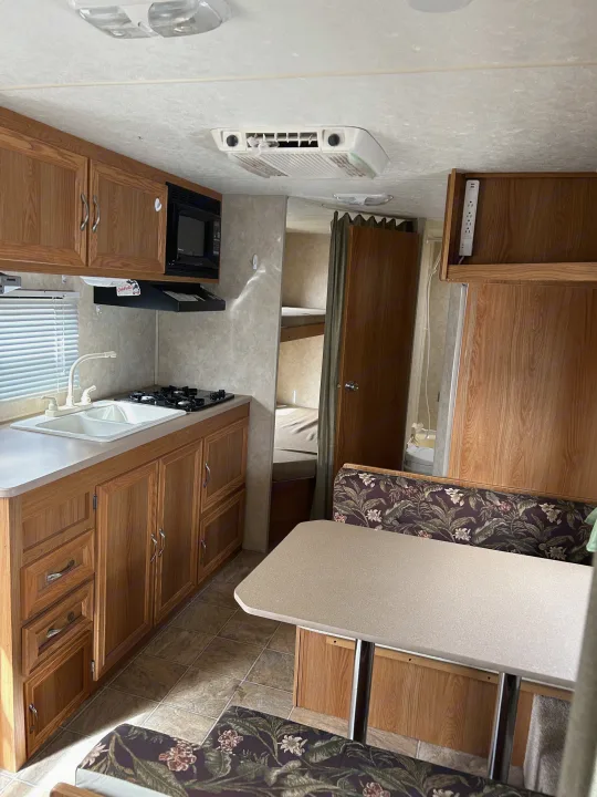 RV rental interior: kitchen with sink & stove, dining booth with floral cushions, and bunk beds visible.. Jag Jag II 2007