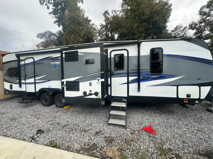 Spacious RV rental, a white, gray, and blue travel trailer, is set up on a gravel lot under cloudy skies.. Forest River X-Lite 2017