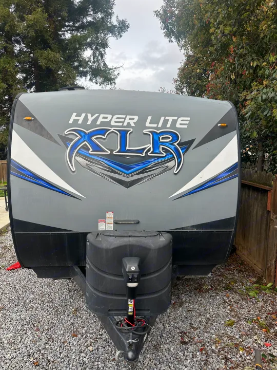 Front view of grey Hyper Lite XLR travel trailer. Great for rv rental, featuring its logo, tongue jack, and gravel parking.. Forest River X-Lite 2017