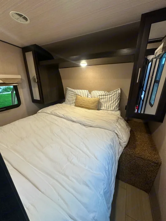 Cozy RV rental bedroom featuring a comfortable bed, striped pillows, overhead storage, and a window with a view outside.. Forest River X-Lite 2017