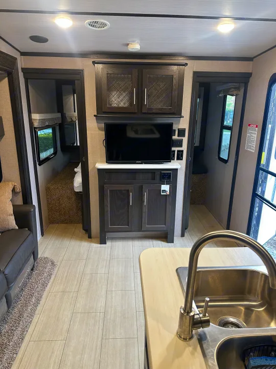 Modern RV rental living space with TV, kitchen sink, and dark wood cabinetry. Includes access to a cozy bedroom area.. Forest River X-Lite 2017