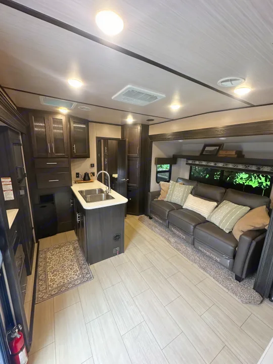 Spacious RV rental interior with modern kitchen island, dark cabinets, and a comfortable leather sofa. Light floors.. Forest River X-Lite 2017
