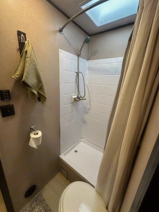 RV rental bathroom featuring a white shower stall, toilet, towel hook, and fan controls.. Forest River X-Lite 2017