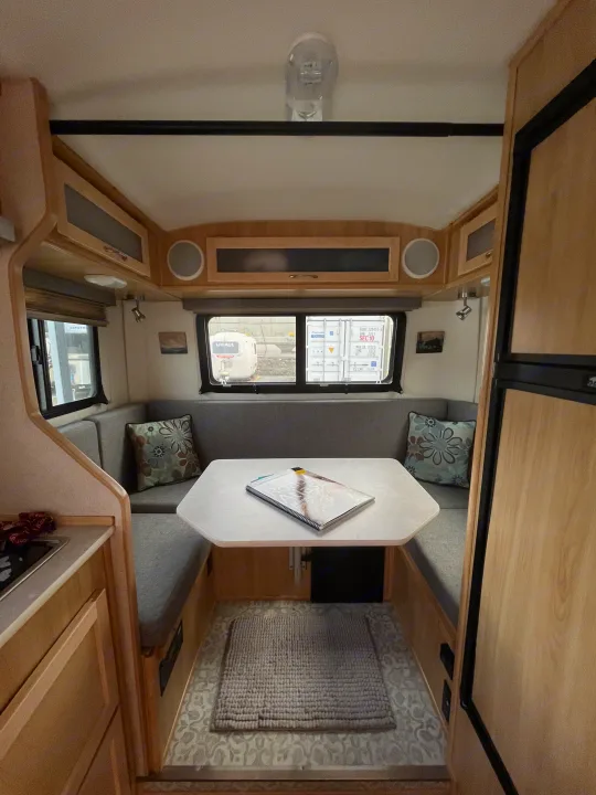 View of a compact RV rental interior with light wood paneling, gray U-shaped dining bench, and a small kitchen.. Escape Trailer Escape Trailer Trailer 2022