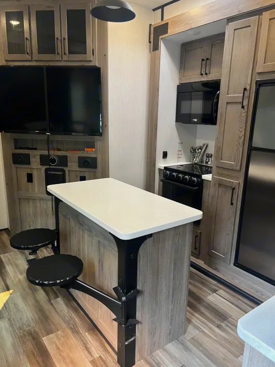 Inside this RV rental: Modern kitchen, dining island with stools, and TV area, all with stylish wood-look finishes.. Heartland RVs Fuel Toy Hauler 2022