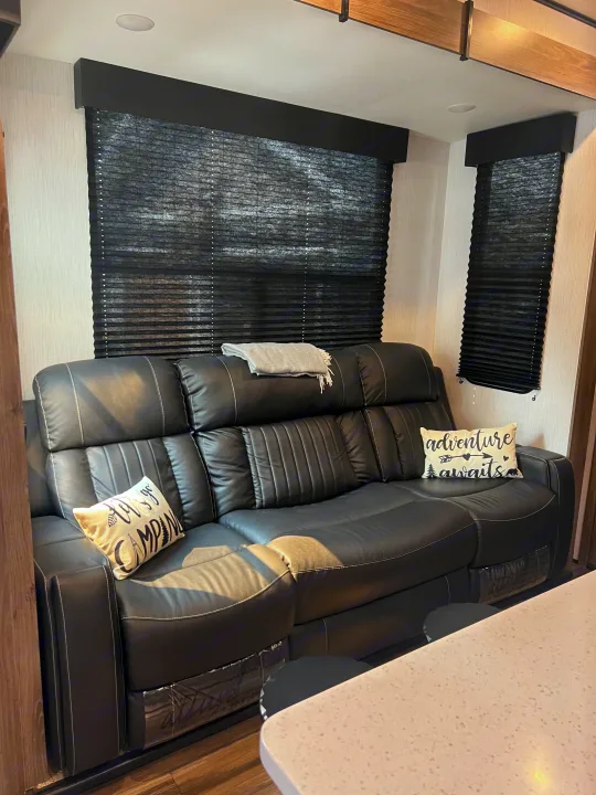 Inviting RV rental: cozy black leather sofa with camping-themed pillows, throw, & dark blinds for comfort.. Heartland RVs Fuel Toy Hauler 2022
