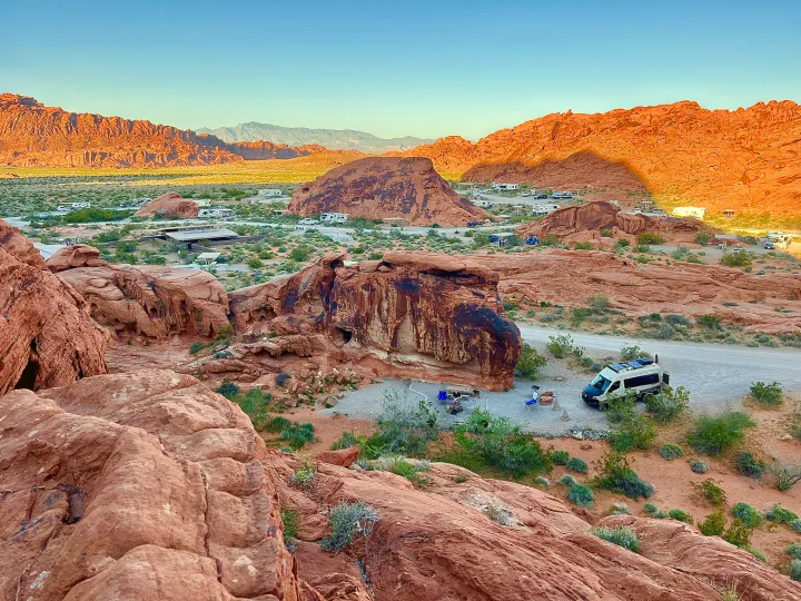 Elevated view of a stunning desert campground with red rock formations, featuring an RV rental and other vehicles.. Winnebago Revel 2023