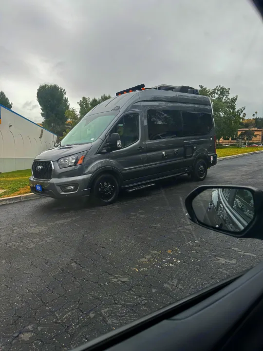 Dark gray Ford Transit rv rental, customized with rooftop solar panels and AC, parked outdoors. Ideal for adventure travel.. Thor Sanctuary 2023