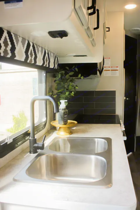 Functional RV rental kitchen with a modern double sink, black faucet, sleek counters, and overhead storage.. Jayco Redhawk 2022