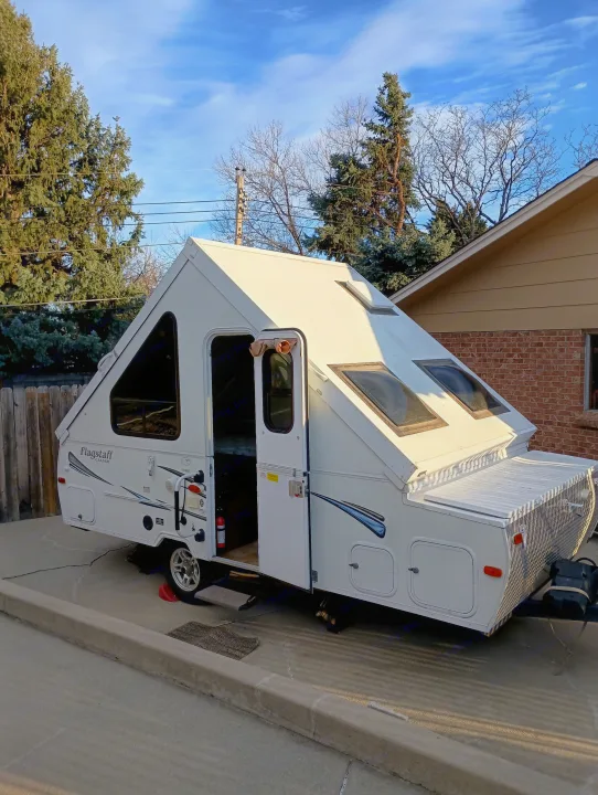 A white Flagstaff A-frame RV rental, fully set up and parked in a driveway, has its door open, revealing the interior.. Forest River Flagstaff Classic 2014