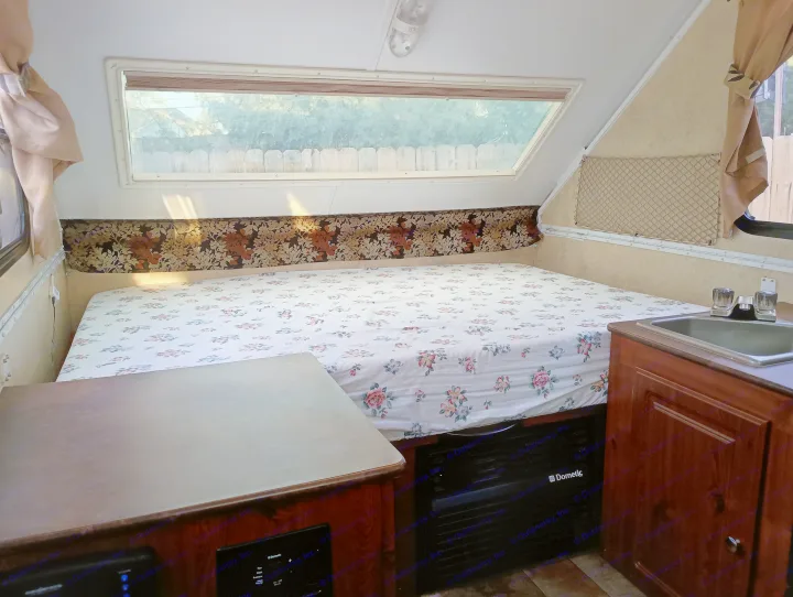 Cozy RV rental interior featuring a floral bed, large window view, and a compact kitchenette with a sink.. Forest River Flagstaff Classic 2014