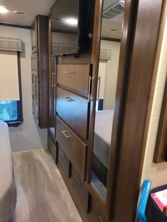 RV rental bedroom: a large wooden wardrobe/dresser with drawers, mirror, and TV.. Entegra Accolade 2020