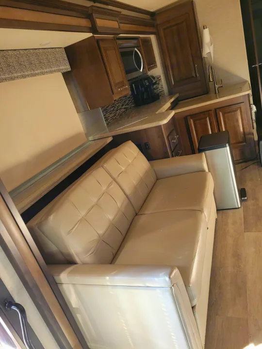 Experience this well-appointed RV rental: a compact kitchen with a microwave and sink, plus a comfy light-colored sofa.. Entegra Accolade 2020