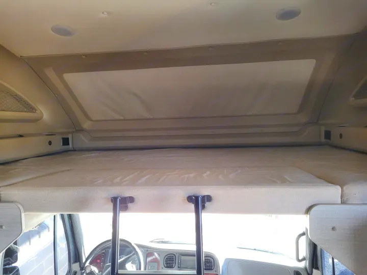 Cozy overhead bunk bed in an RV rental, with a view of the driver's cab and dashboard visible below.. Entegra Accolade 2020