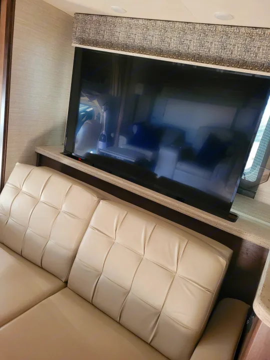 Cozy RV rental living area with a comfortable beige sofa and a pop-up TV for entertainment.. Entegra Accolade 2020