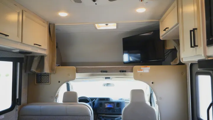 Spacious RV rental interior featuring a front cabin, overhead bunk with a TV, and ample storage cabinets.. Thor Motor Coach Freedom Elite 2022