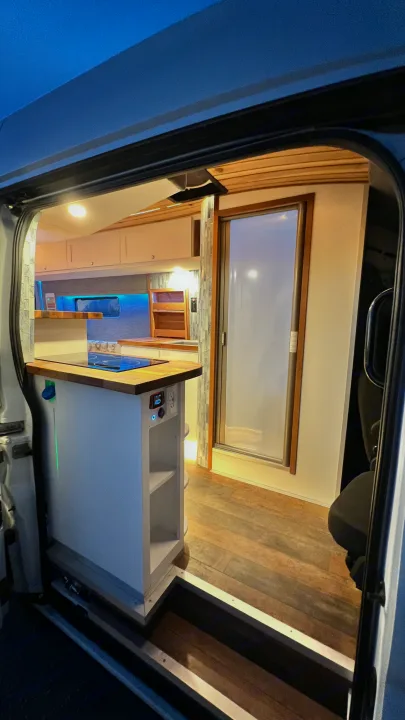 Modern RV rental interior: compact kitchen with induction cooktop, wood finishes, and clever storage for mobile living.. Ford Transit 2019